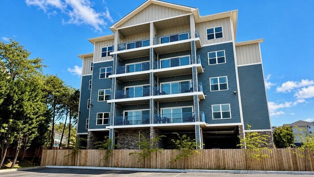 A multi-story residential building with balconies, a parking lot, and a wooden fence. - New Pige Forge Condo | Mtn View - Walk Everywhere (Pigeon Forge)
