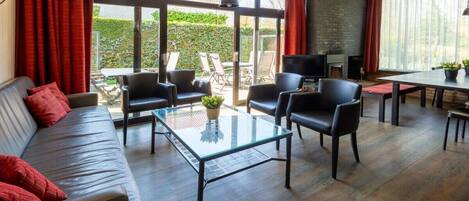 A modern living room with a sofa, chairs, a glass coffee table, and a TV.