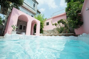 A swimming pool with a pink building in the background. - Qiran Rustic Resort Villa (Huairou)