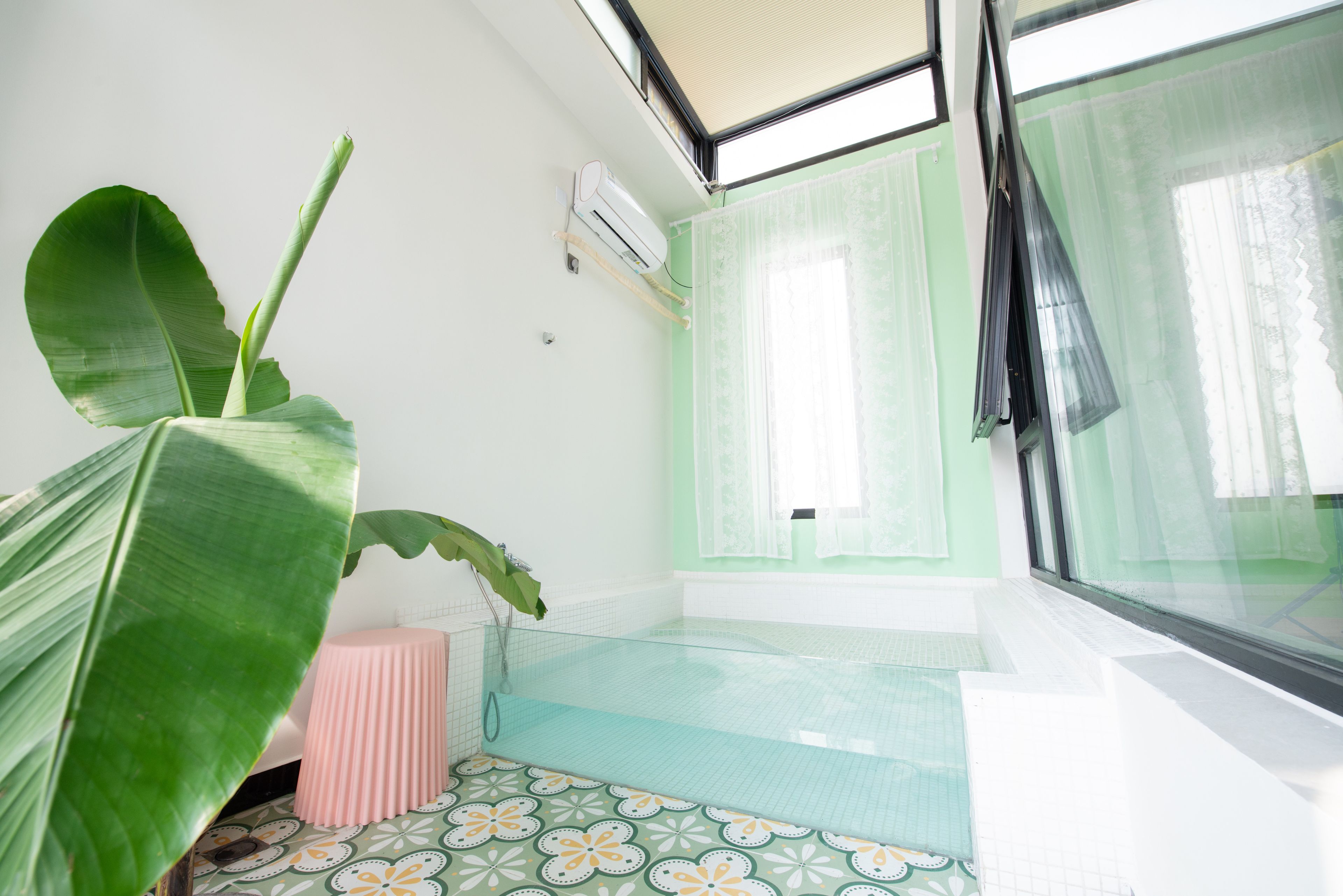 Ein Badezimmer mit Dusche, einer großen Grünpflanze und einem Fenster mit transparenten Vorhängen.