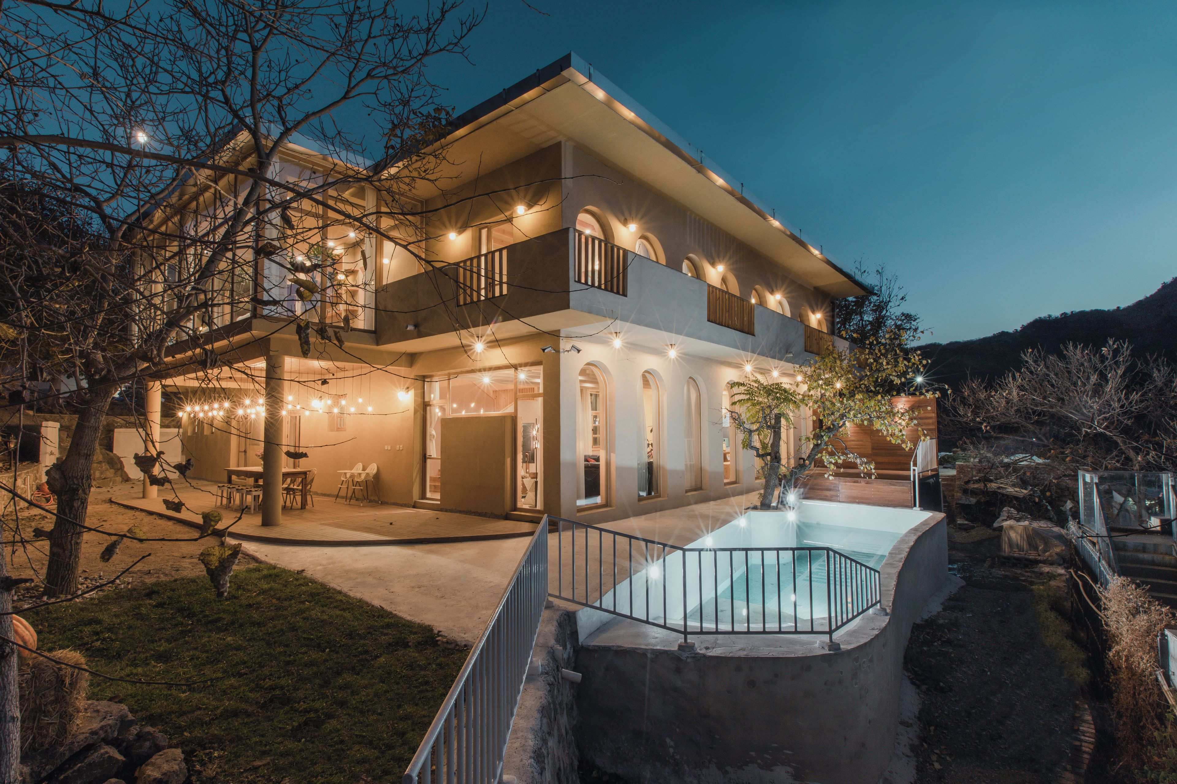 Una casa de dos pisos con piscina, mobiliario exterior y luces colgantes.