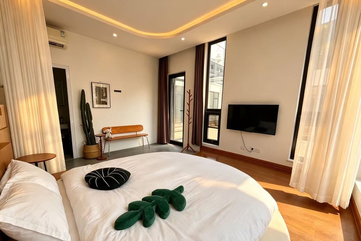 Un dormitorio con una cama grande, televisor y ventana con cortinas.