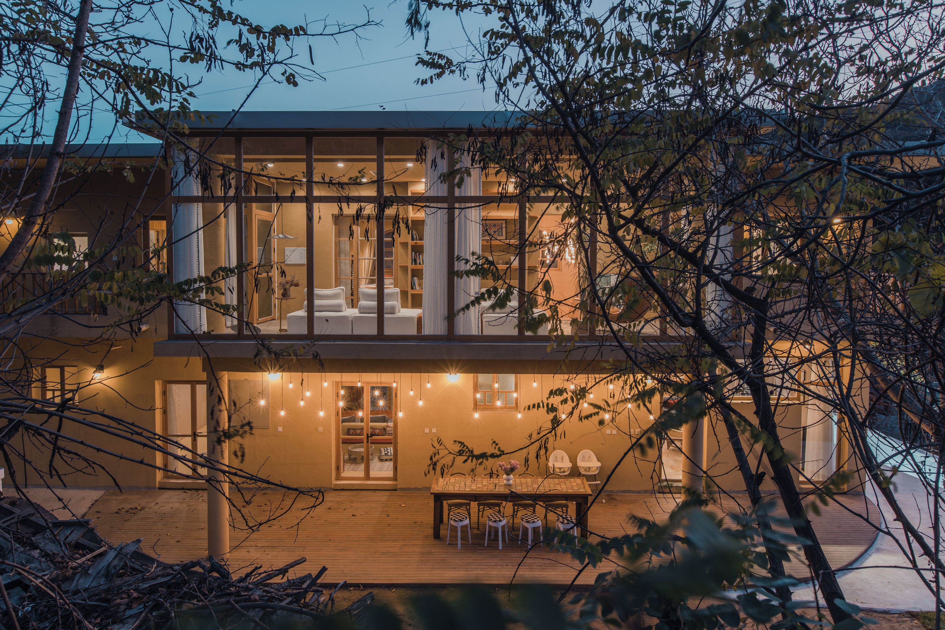 A modern two-story house with a balcony, a dining area with a table and chairs, and a view of the surrounding trees.