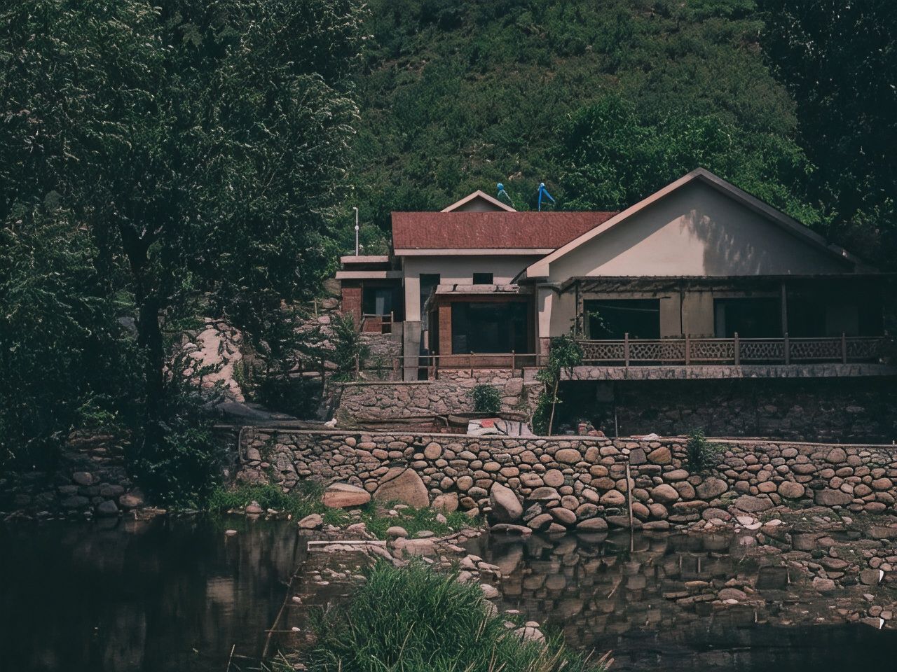 Una casa con un muro in pietra e uno stagno di fronte.