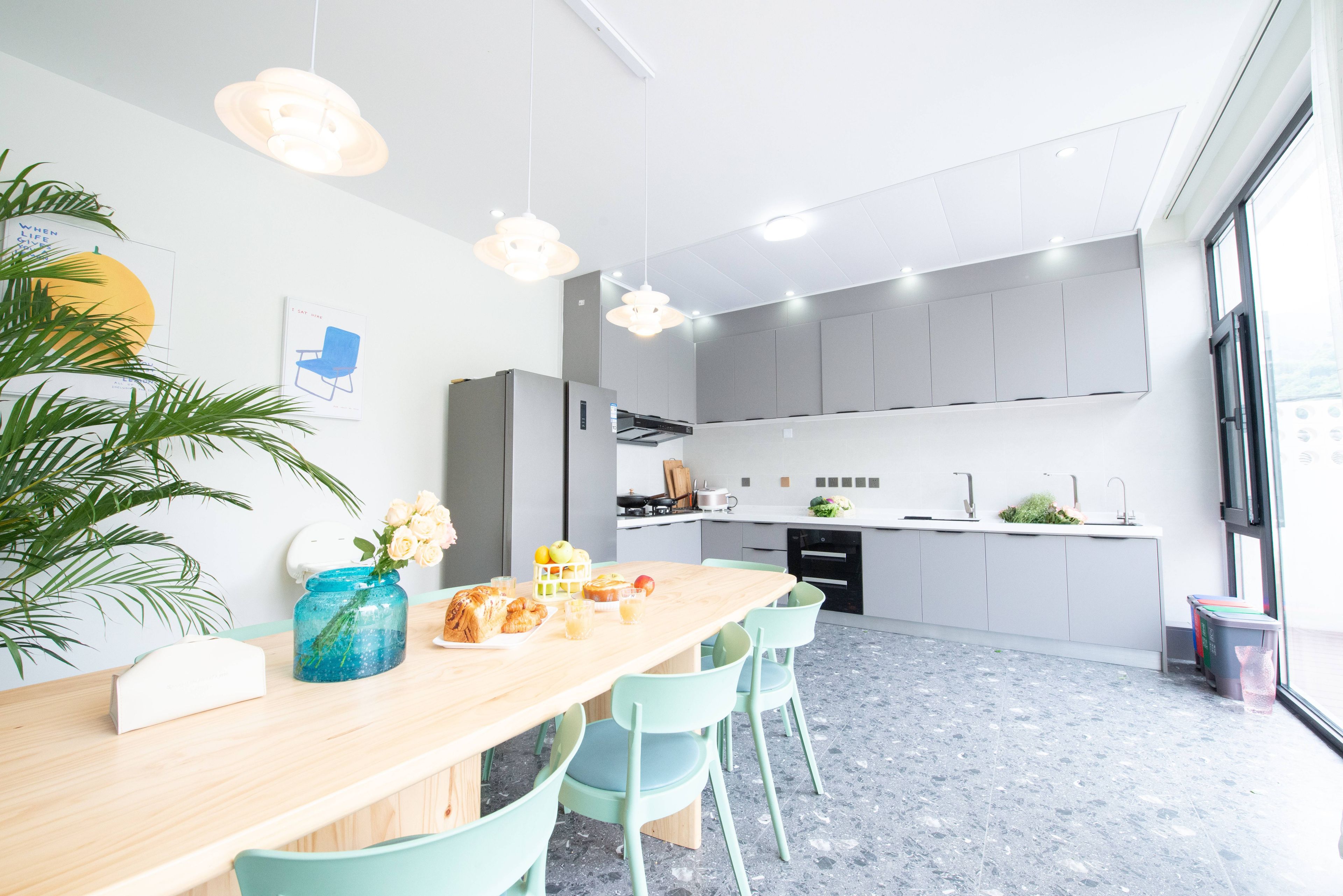 Una cucina moderna con mobili grigi, un piano di lavoro in legno e un'area pranzo con tavolo in legno e sedie verde chiaro.
