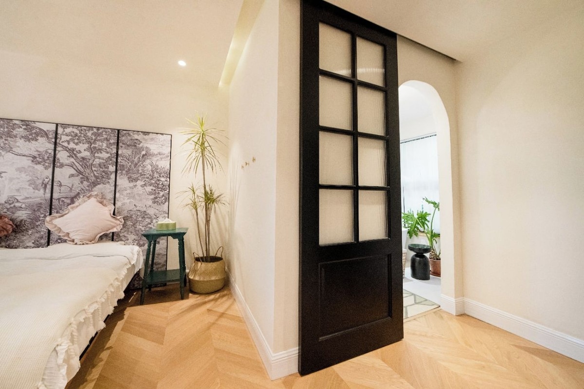 Un dormitorio con cama, un ventanal grande y una puerta con paneles de vidrio esmerilado.