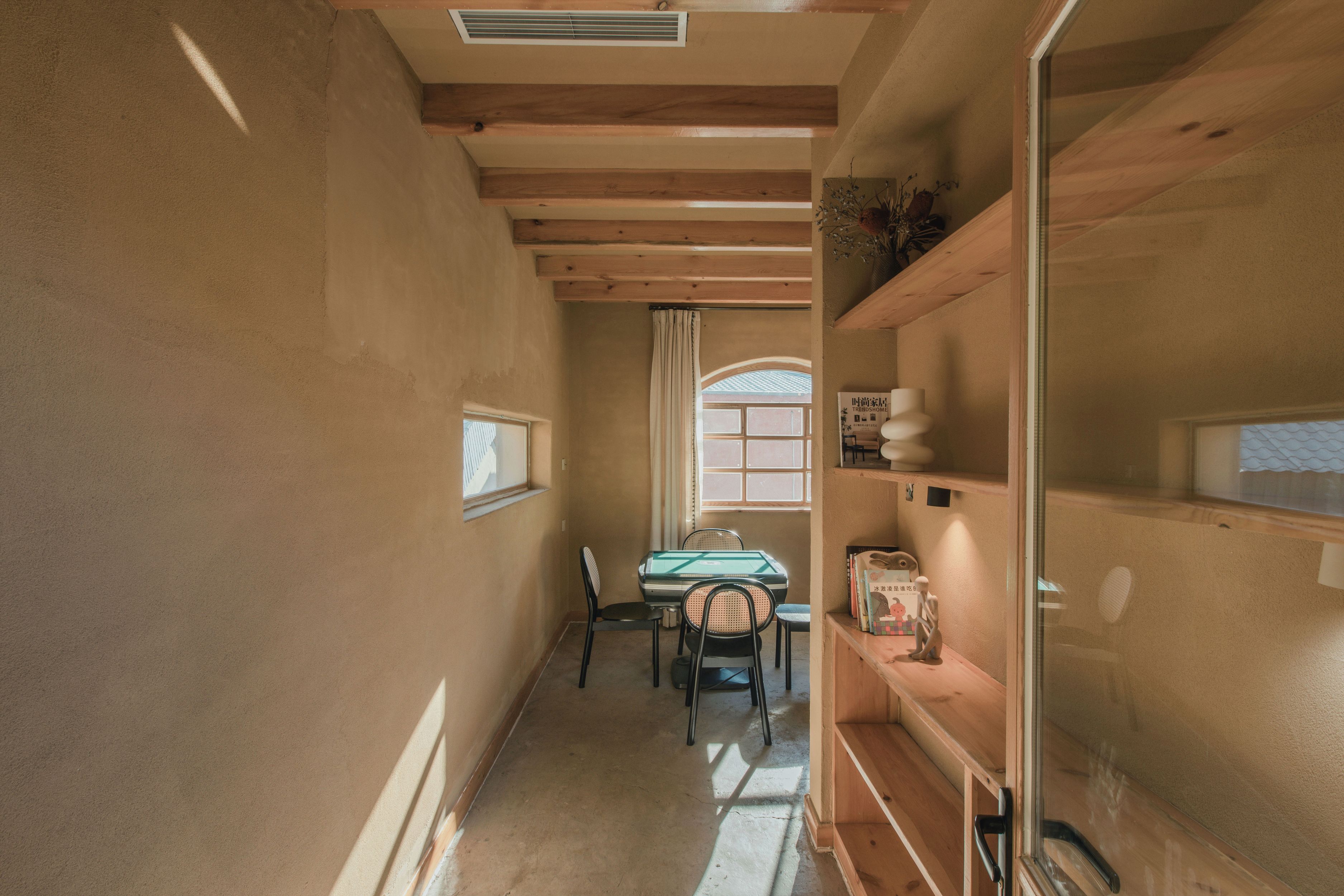A narrow hallway with wooden beams, a dining area with a table and chairs, and a window with a view.