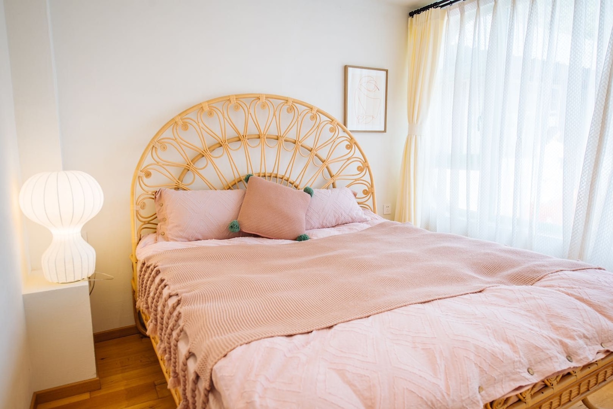 Una cama con cabecera trenzada, una lámpara de noche y un cuadro en la pared.