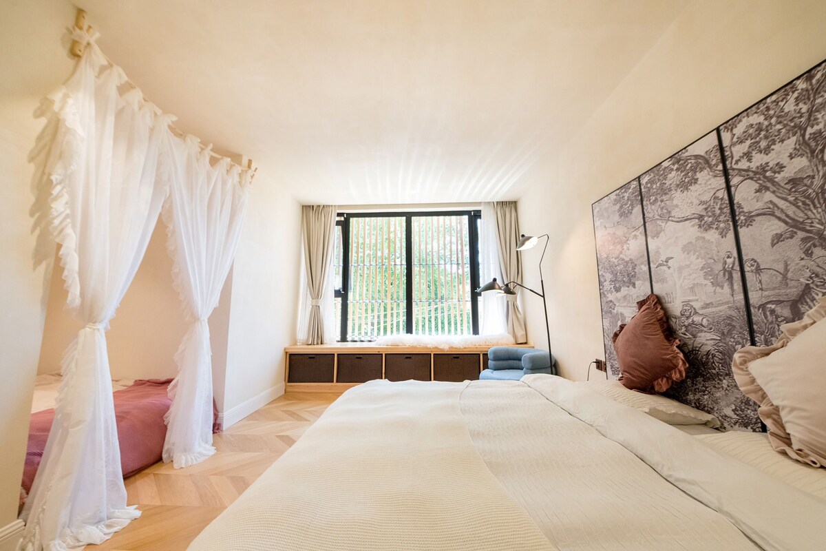 Un dormitorio con una cama grande, una ventana con persianas, una mesita de noche y un cabecero con estampado floral.