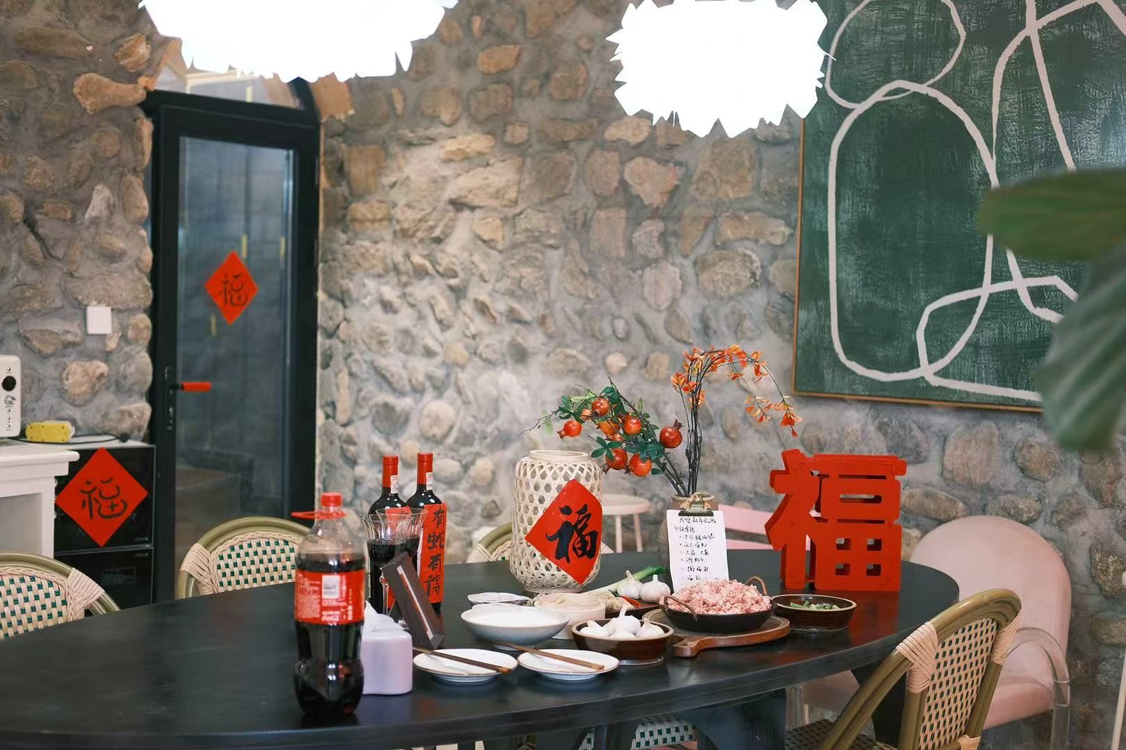 Un tavolo imbandito con diversi piatti, bottiglie e oggetti decorativi in una stanza con pareti in pietra e una porta decorata di rosso.
