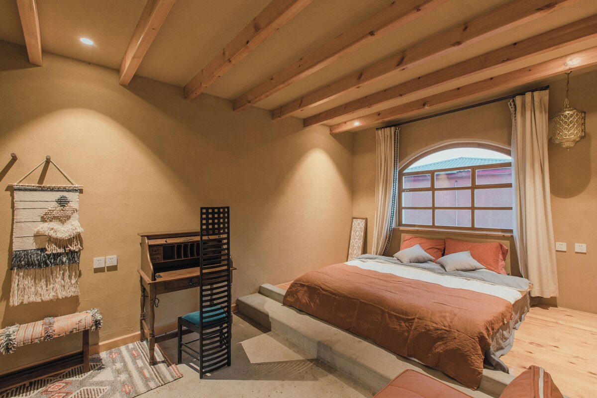 Un dormitorio con cama, escritorio, silla, ventana con cortinas y lámpara colgante.