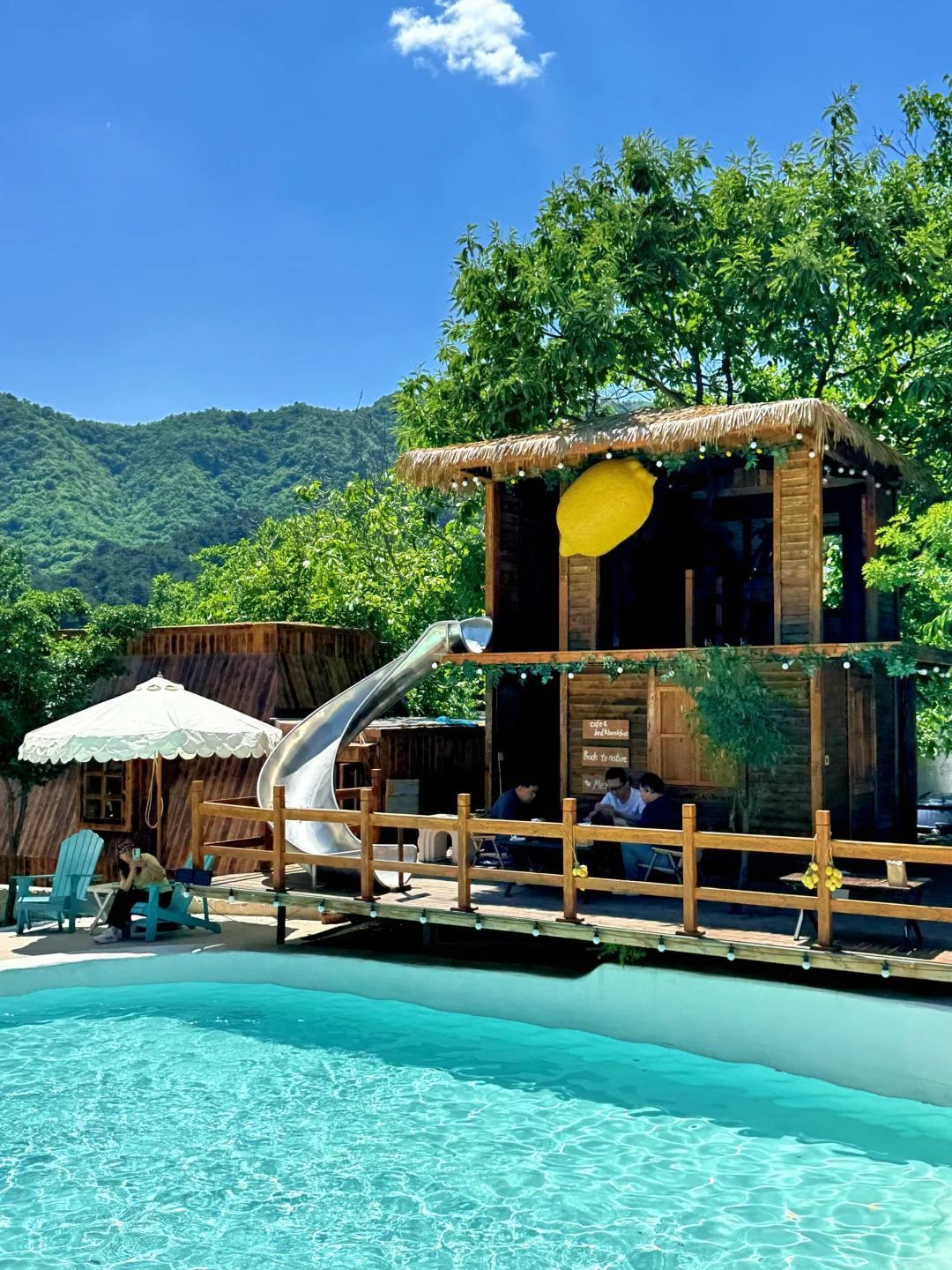 Una cabaña de madera con techo de paja, un tobogán y una piscina.