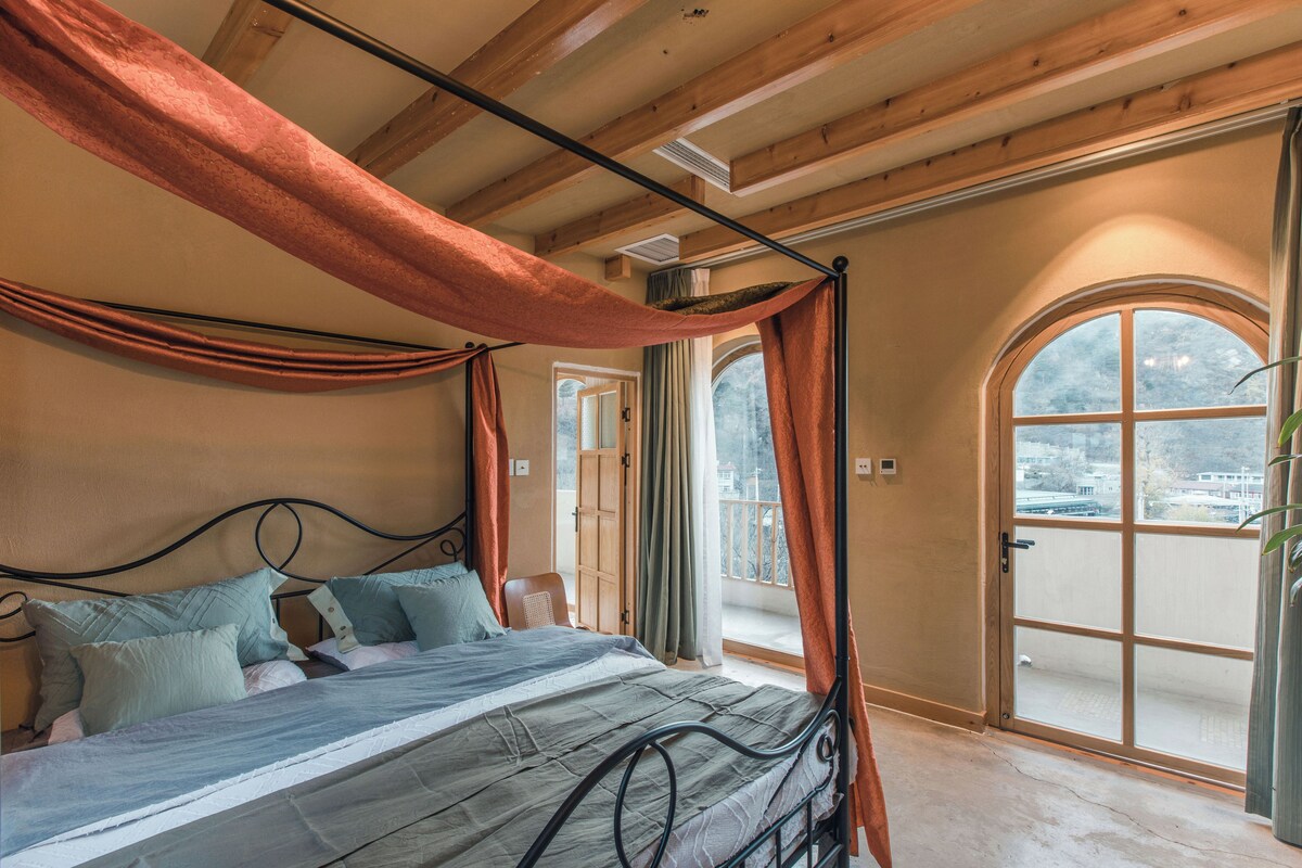 Un dormitorio con cama con dosel, un amplio ventanal de arco y vistas al exterior.