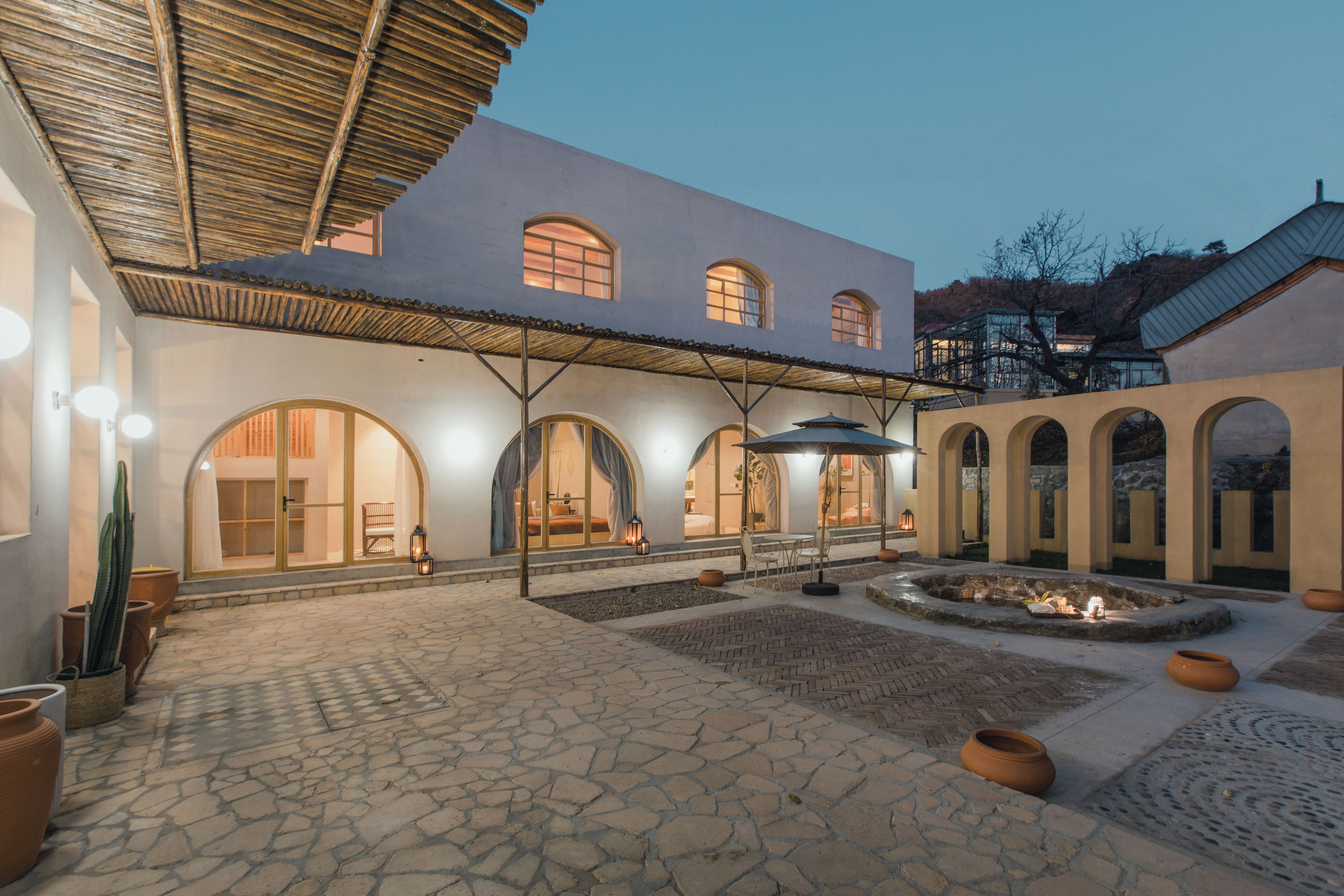 Un patio con suelo de piedra, ventanas de arco y una zona de estar cubierta.