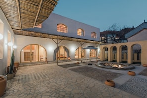Un patio con suelo de piedra, ventanas de arco y una zona de estar cubierta.