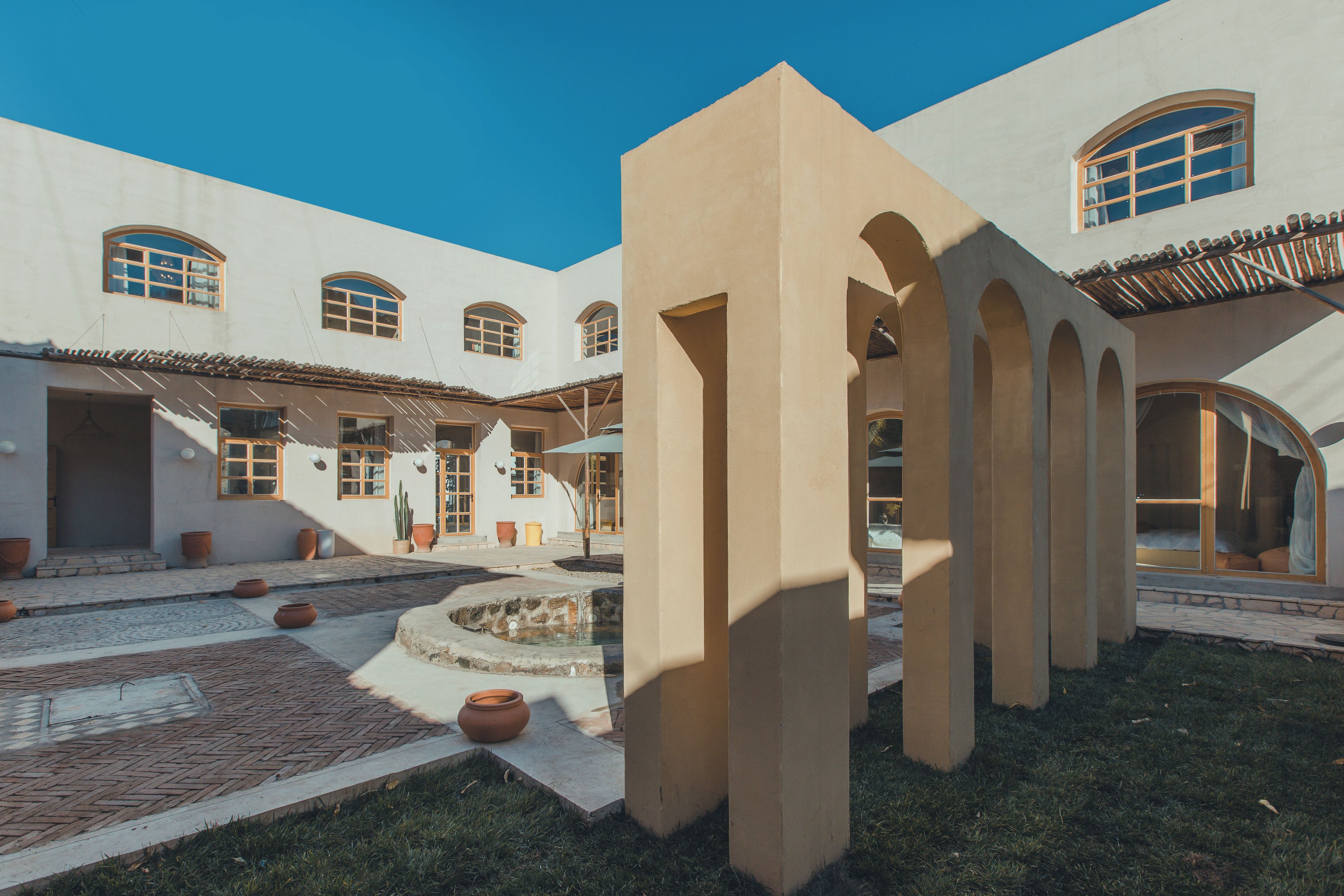 A courtyard with a fountain, potted plants, and a building with arched windows and doors.