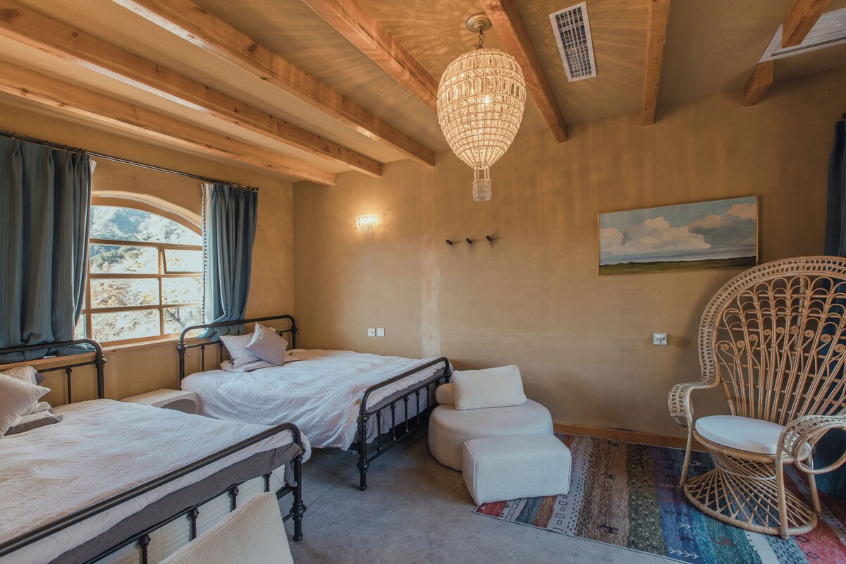 Un dormitorio con dos camas, una lámpara colgante, una silla y un cuadro en la pared.