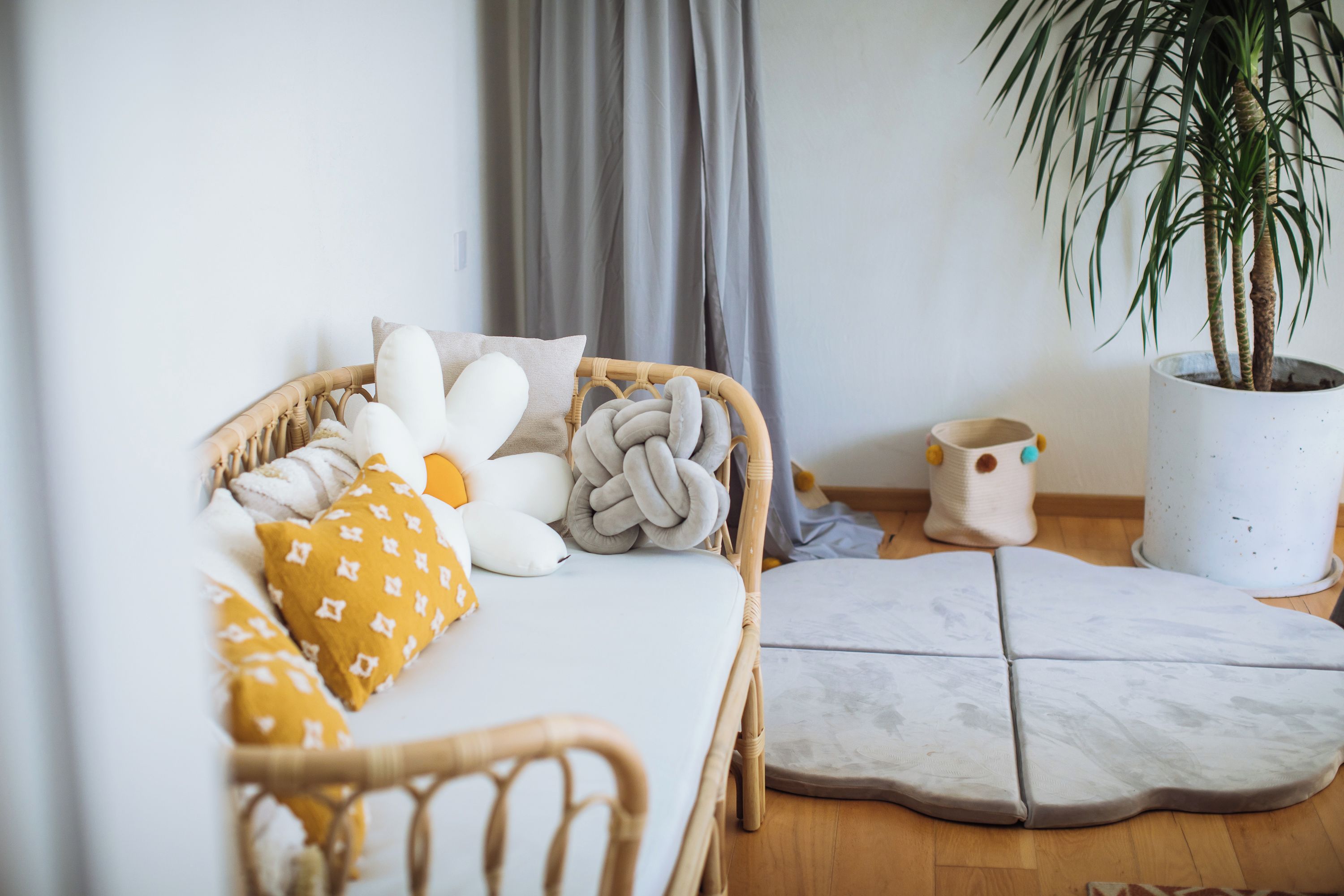 Una stanza con un letto, una sedia in vimini, una pianta in vaso e un tavolino.