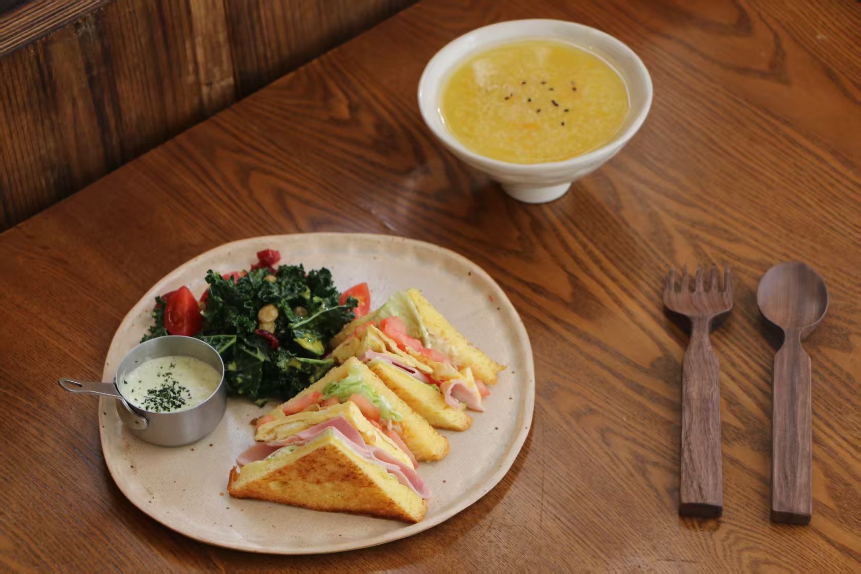 A plate with a sandwich, soup, and a small bowl of sauce on a wooden table.