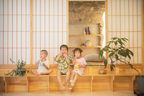 Three children sitting on a wooden bench in a room with tatami mats, a stone shelf, and a potted plant. - Qiran Rustic Resort Villa (Huairou)