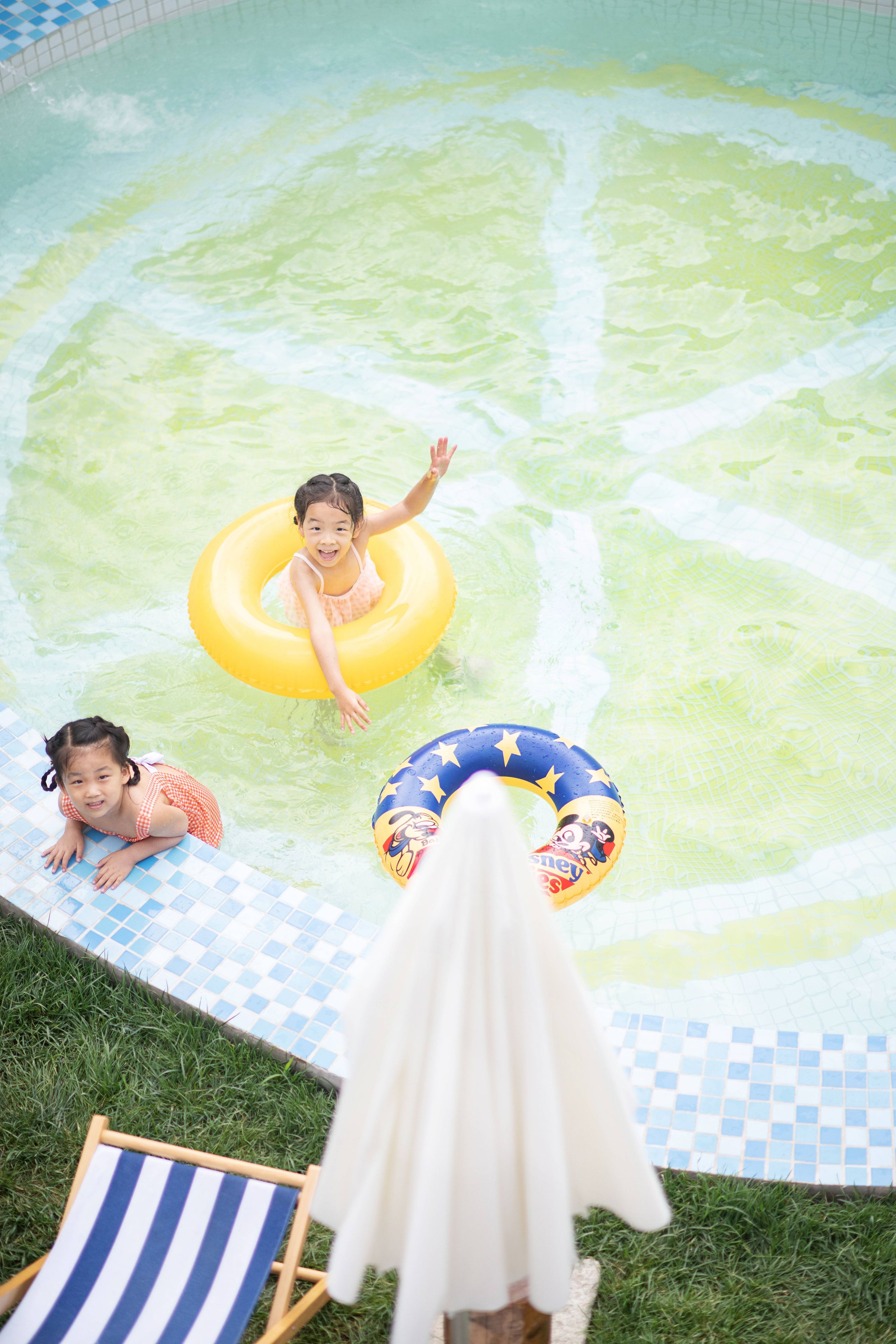 A swimming pool with two children playing, one in a yellow float and the other in a blue float.