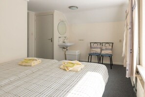A hotel room with two beds, a bathroom with a sink, and a chair. - Holiday apartment with 1 bedroom (Zoutelande)