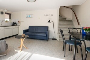 A modern living space with a sofa, dining table, chairs, a coffee machine, and a staircase. - Holiday apartment with 1 bedroom (Zoutelande)