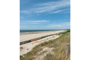 A beach with a row of beach huts and a clear sky. - Holiday apartment with 1 bedroom (Zoutelande)