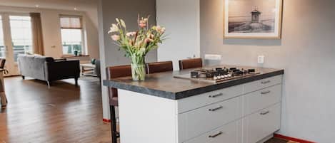 A modern kitchen with a marble countertop, white cabinetry, and a vase of flowers.