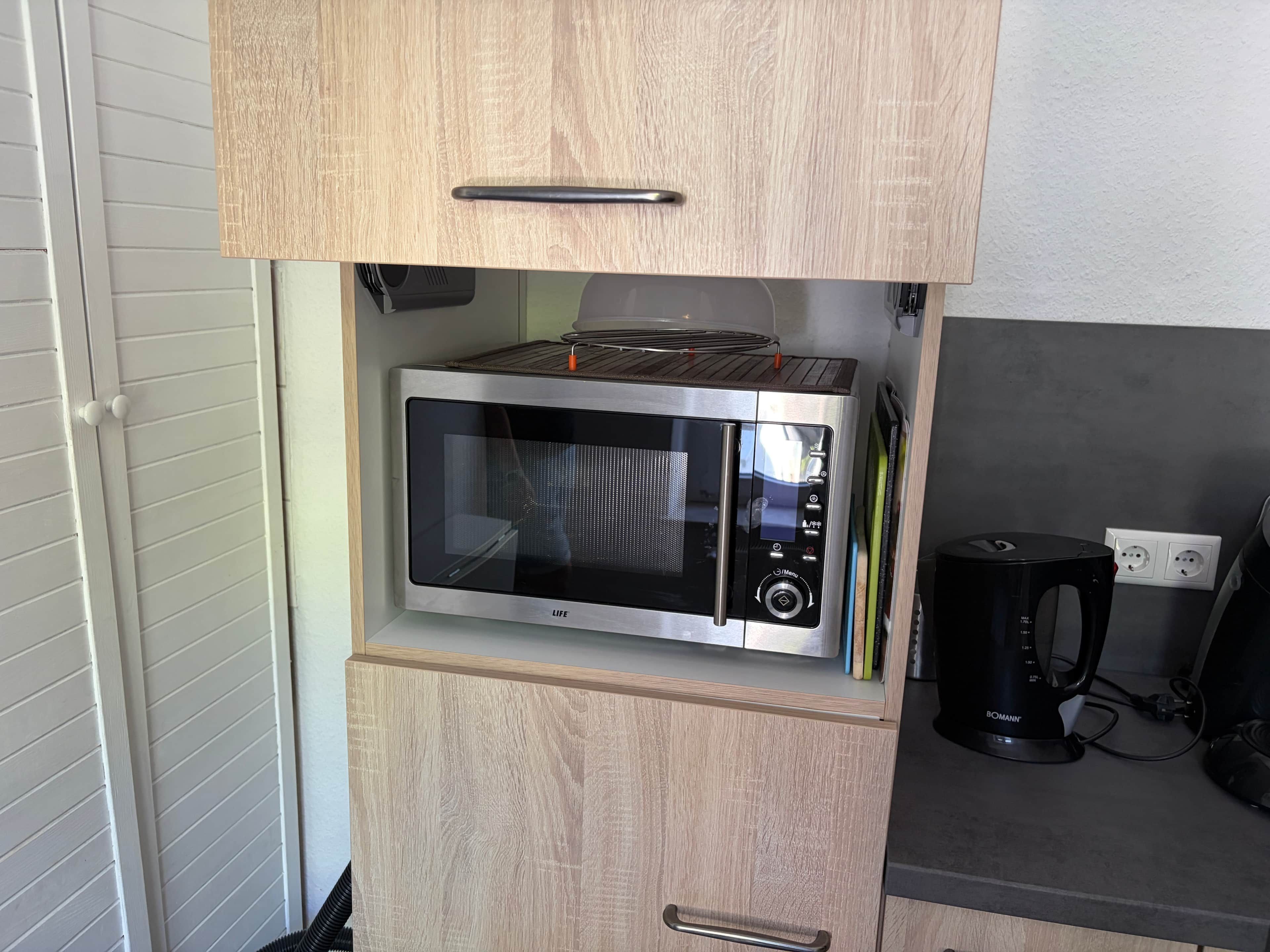 Een compacte magnetron met een digitaal display en bedieningspaneel, ingebouwd in een houten kast met een handgreep.