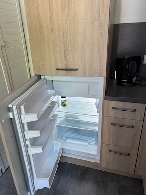 Un refrigerador obert amb diverses prateleires, una ampolla d'oli d'oliva i una cafetera a la tauleta.