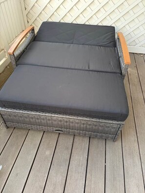 Ein Korbssessel mit schwarzem Kissen auf einer Holzterrasse.