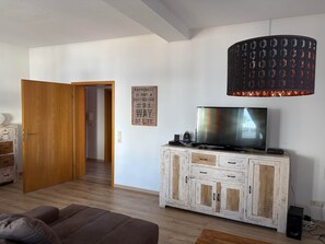 Ein Wohnzimmer mit Fernseher auf einer Kommode, einer Tür zu einem anderen Raum und einer Wand mit einem motivierenden Zitat.
