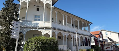 A white building with 'Minna' on the facade, featuring a balcony and a signpost with various directions.