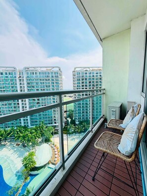 A balcony with a view of a swimming pool and palm trees, a wicker chair, and a small table. - 2BR Tropical Scandi Suite (Parañaque)