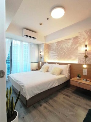 A modern bedroom with a large bed, bedside tables, a wall-mounted light fixture, and a potted plant. - 2BR Tropical Scandi Suite (Parañaque)