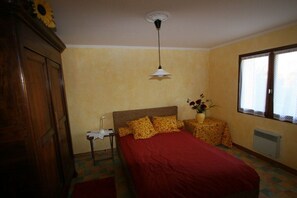 A bedroom with a bed, a nightstand, a wall-mounted lamp, a window with blinds, and a radiator. - Holiday home in Serignan with swimming pool (Serignan)