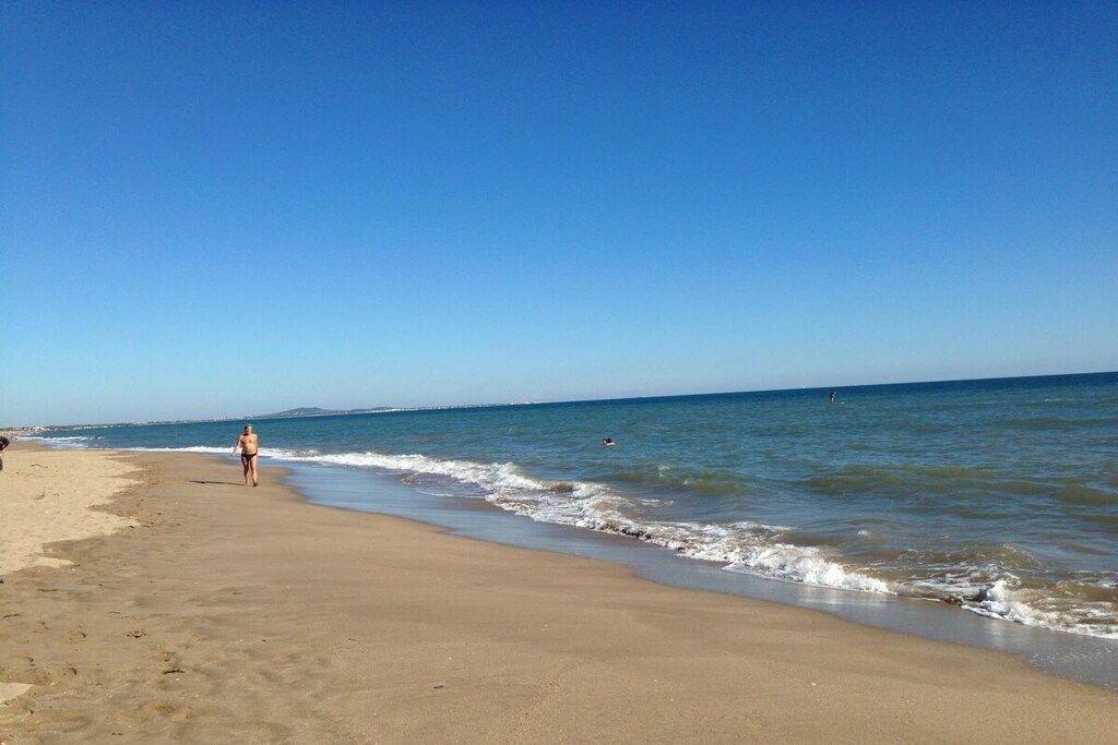 Une plage avec un ciel dégagé, une mer calme et une personne qui se promène le long du rivage.