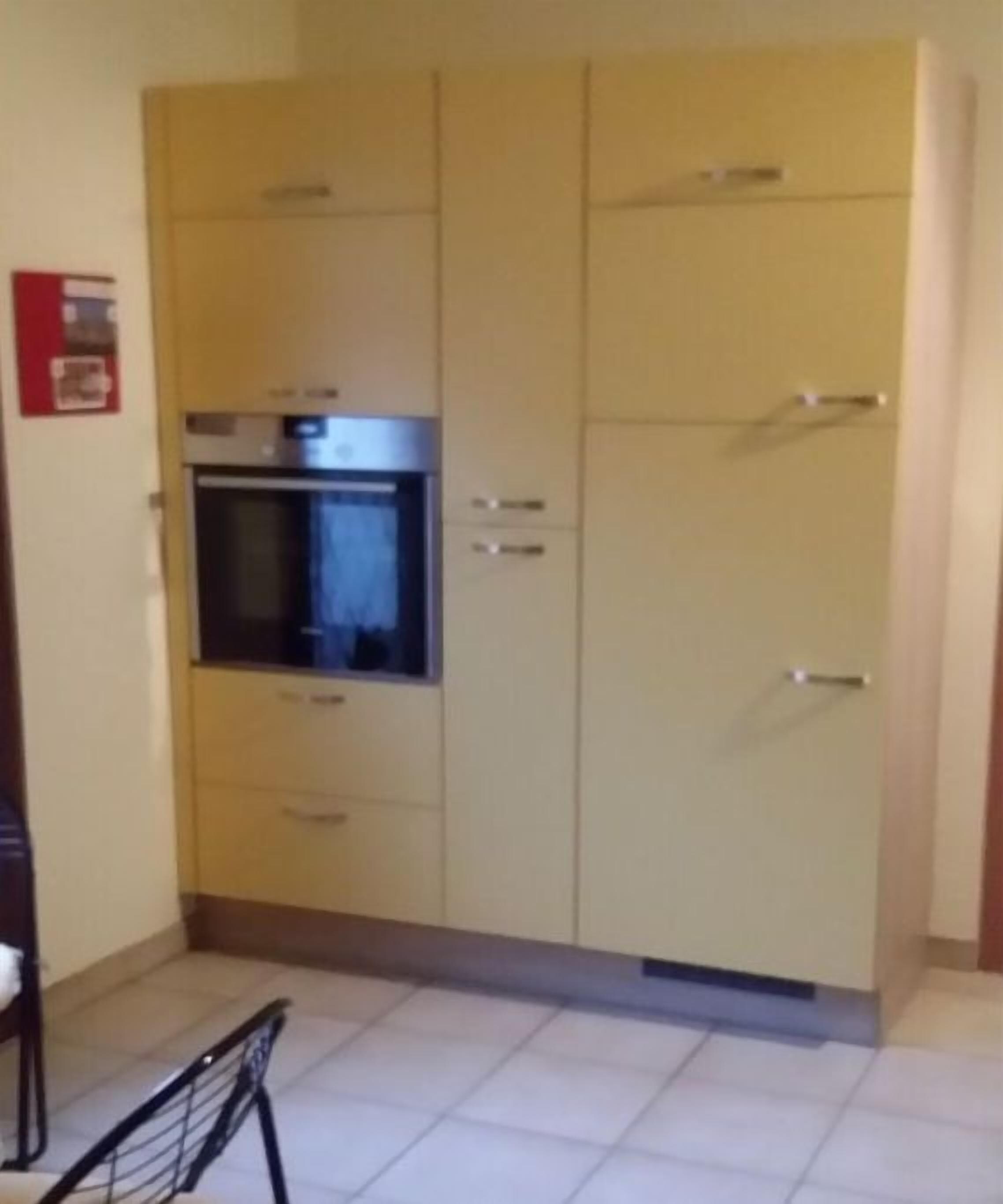 Een keuken met een inbouwoven en magnetron, een kast met lades en een betegelde vloer.