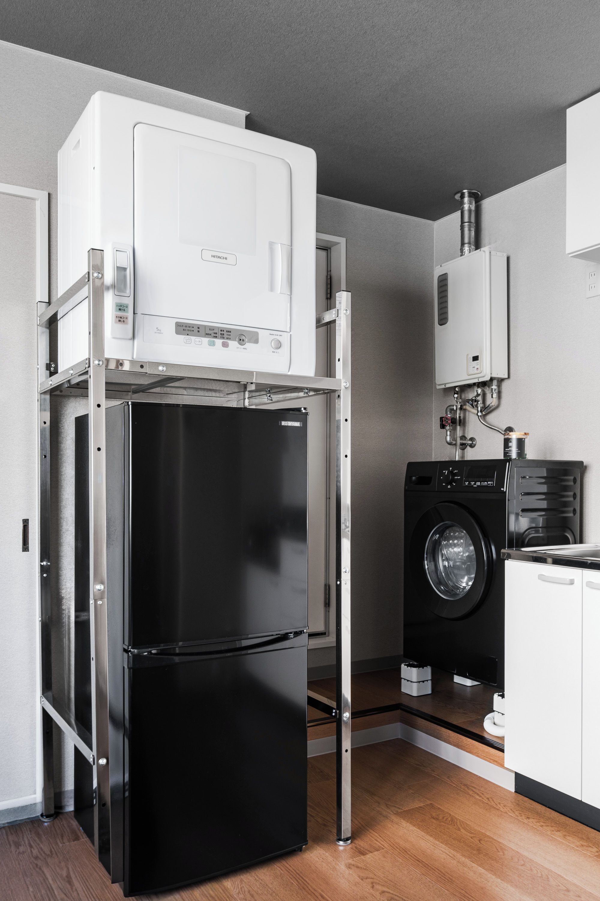 Cozinha compacta com geladeira preta, máquina de lavar e armário branco.