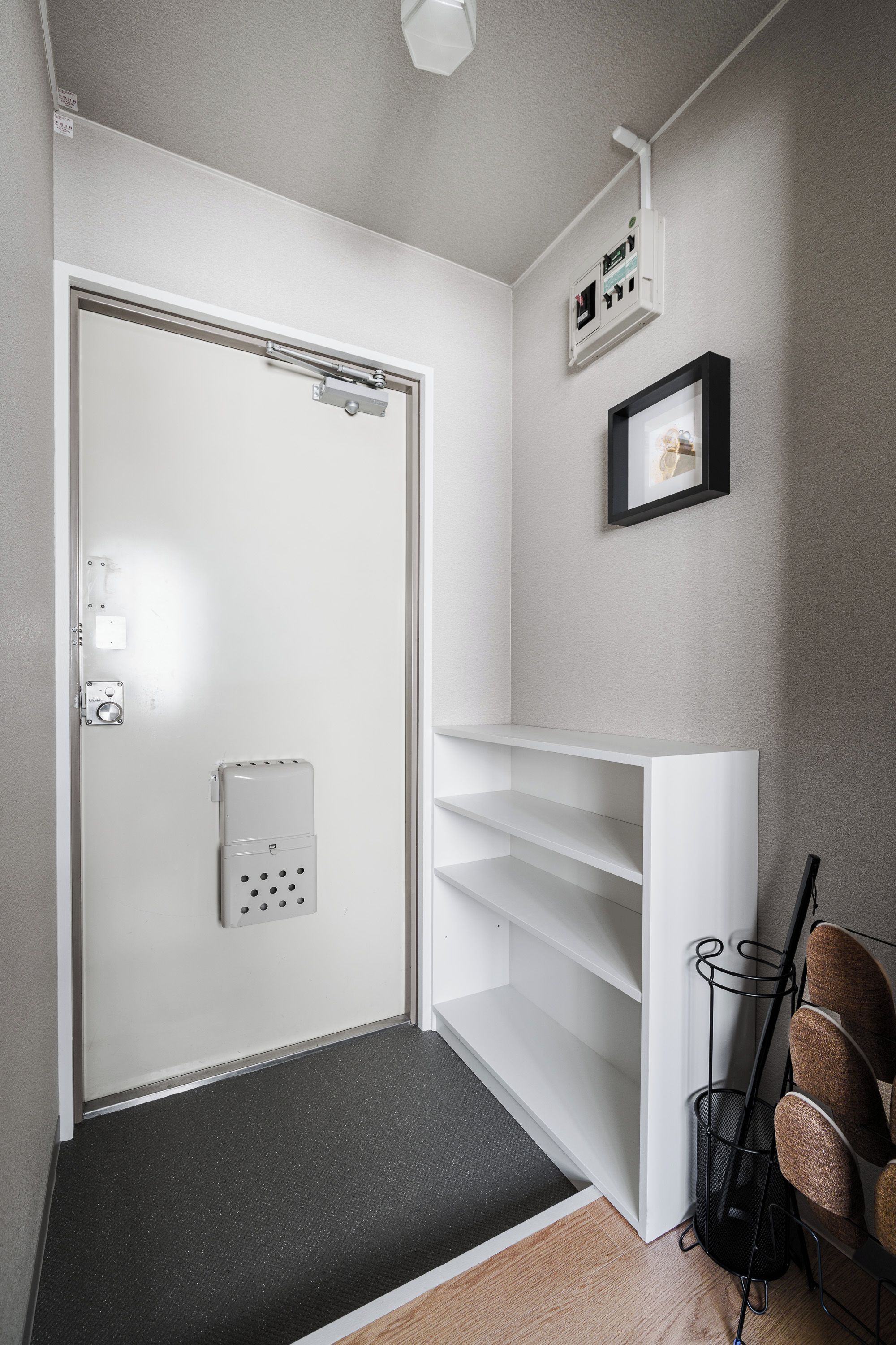 Um corredor com porta branca, tapete preto, estante branca e cadeira preta.