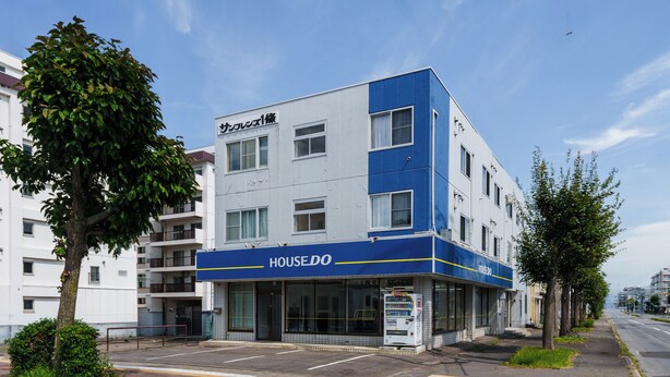 A modern building with a blue and white facade, a visible entrance, and a vending machine on the ground floor. - SUN FRIENDS 201 (Asahikawa)
