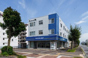 A modern building with a blue and white facade, a visible entrance, and a vending machine on the ground floor. - SUN FRIENDS 201 (Asahikawa)