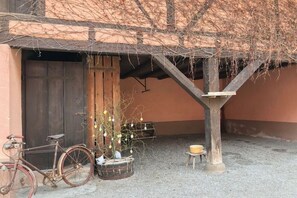 A rustic building with a wooden door, a bicycle, a plant in a barrel, and a small stool. - Holiday apartment with 1 bedroom (Jebsheim)