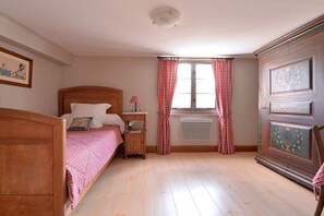 A bedroom with a wooden bed, a nightstand, a radiator, and a window with curtains. - Holiday apartment with 1 bedroom (Jebsheim)
