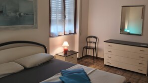 Une chambre à coucher comprenant un lit, un bureau, une chaise, une commode, une lampe et un tableau accroché au mur.