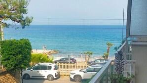 Un balcon avec vue sur la mer, un espace de stationnement avec des voitures et quelques plantes.