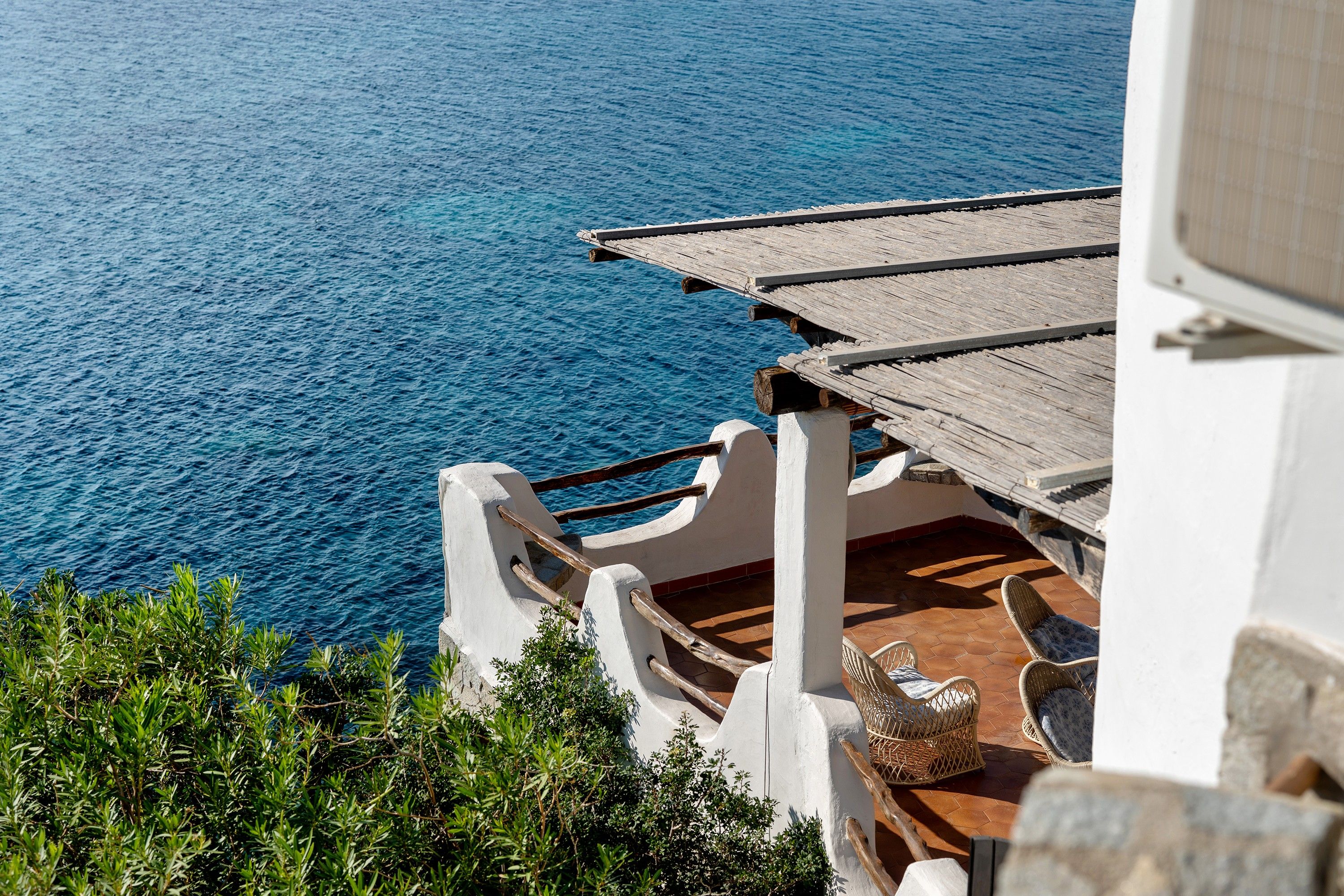 Une propriété située en bord de mer, dotée d’une terrasse en bois offrant une vue sur l’océan, d’un escalier en pierre et d’une chaise en osier.
