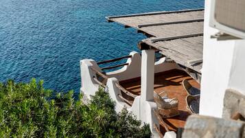 Une propriété située en bord de mer, dotée d’une terrasse en bois offrant une vue sur l’océan, d’un escalier en pierre et d’une chaise en osier.