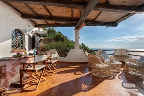 An outdoor terrace with hexagonal tiles, wicker furniture, and a view of the sea.